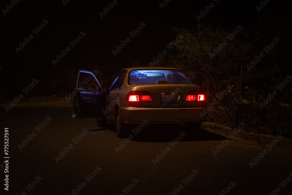 Carro sedan plomo antiguo vacío en una autopista con la puerta abierta y las luces prendidas roja y azul