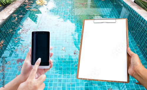 Smartphone and blank paper on wooden clipboard in girl hand over dirty pool water background, pool service and maintenance