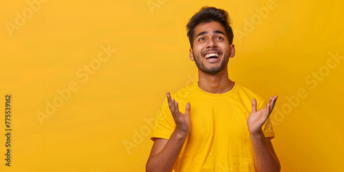 Emotion of joy, celebration of victory. Handsome Indian man is sincerely happy, looking to the side and making a winning gesture while standing against a yellow background. Copy space photo