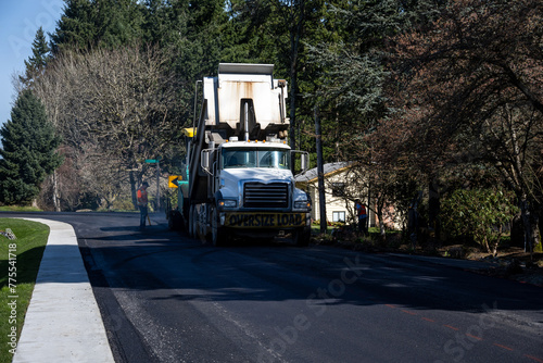 Dump truck with fresh hot asphalt feeding into an asphalt paving machine in the early morning, road re-paving construction project
