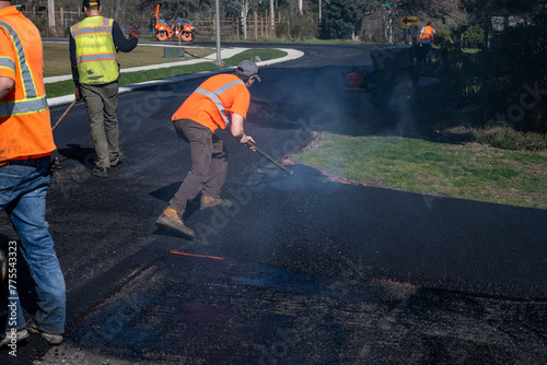 Road re-paving construction project, construction worker with asphalt rake smoothing out fresh blacktop on driveway
