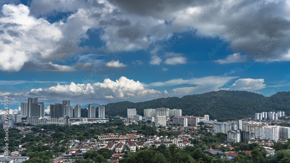 Panorama of the modern city. Skyscrapers against a background of blue sky and clouds. A buildings among the green vegetation. Hills in the distance. Georgetown. Penang. Malaysia. Panorama of the modern city. Skyscrapers against a background of blue sky and clouds. A buildings among the green vegetation. Hills in the distance. Georgetown. Penang. Malaysia.