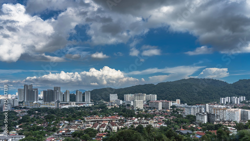 Panorama of the modern city. Skyscrapers against a background of blue sky and clouds. A buildings among the green vegetation. Hills in the distance. Georgetown. Penang. Malaysia.