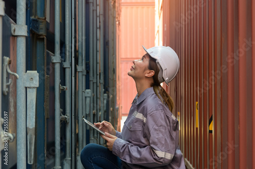 Industrial engineer checking containers with digital tablet in logistic shipping cargo yard. Asian female worker in uniform with white helmet inspect container.