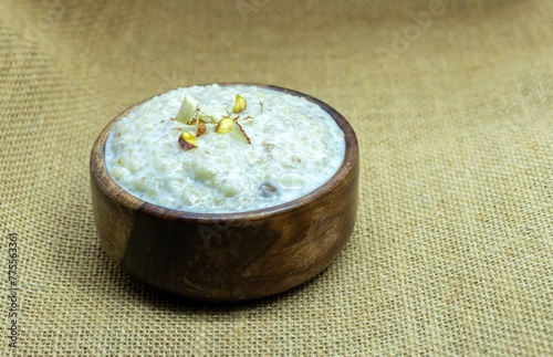 Cracked Wheat Kheer or Payesh Garnished with Cashew, Almond, Pistachio in a Wooden Bowl Isolated on Bulap Fabric Background with Copy Space, Also Known as Ksheeram, Milk Pudding photo