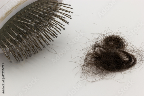 Hair brush next to a pile of brown hair on a white background. This image can be used to illustrate topics related to hair loss, medical treatments and aging. (ID: 775576775)