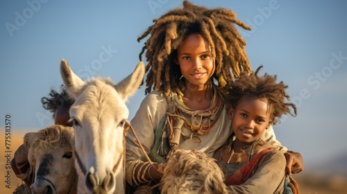 African children with dreadlocks from the nomadic Wodaabe tribe, sitting on the backs of a donkey during the moving season against the blue sky.