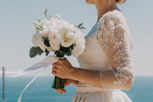 bride is holding a bouquet of white flowers. The bouquet is large and has a lot of flowers in it. The woman is wearing a white dress and a gold ring on her finger. Scene is elegant and romantic. © svetograph