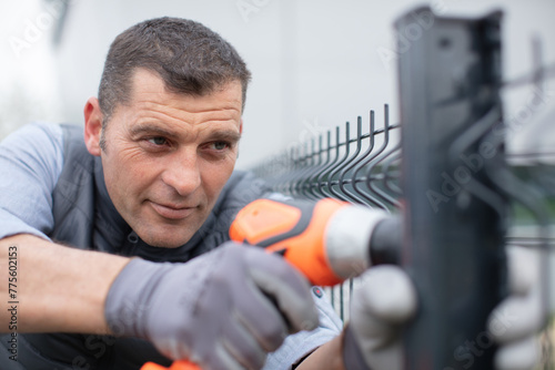 construction man working with cordless electrical screwdriver on metal fence photo