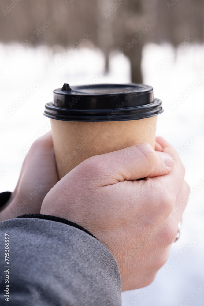 Male hands holding paper cup with coffee on snow background.