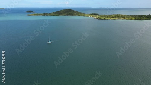 Aerial clip of a catamaran on the calm ocean, tropical islands and sunshine behind. photo