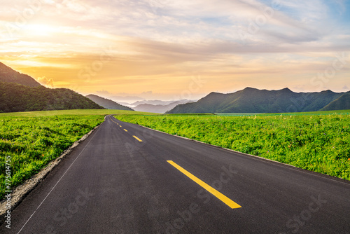 Asphalt highway road and green meadow with mountain nature landscape at sunset