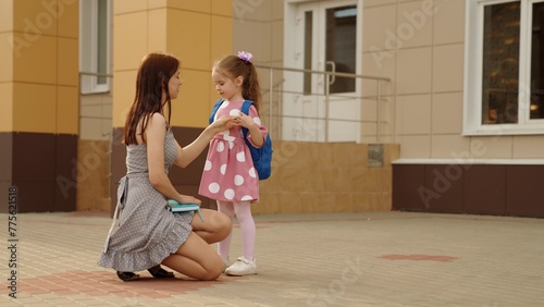 Smiling young mother meeting cute daughter pupil from school first lesson hugging with love. Happy family mom and girl kid child meet up after classroom elementary education embracing positive emotion