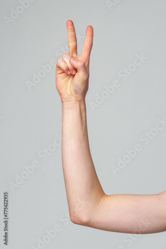 Close-Up of a Persons Arm Showing a Peace Sign Against a Grey Background