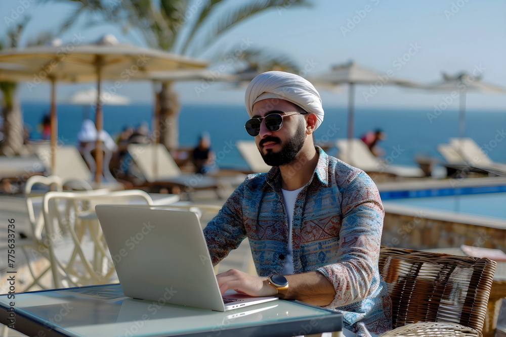 young arabian man working on a laptop in a beach bar