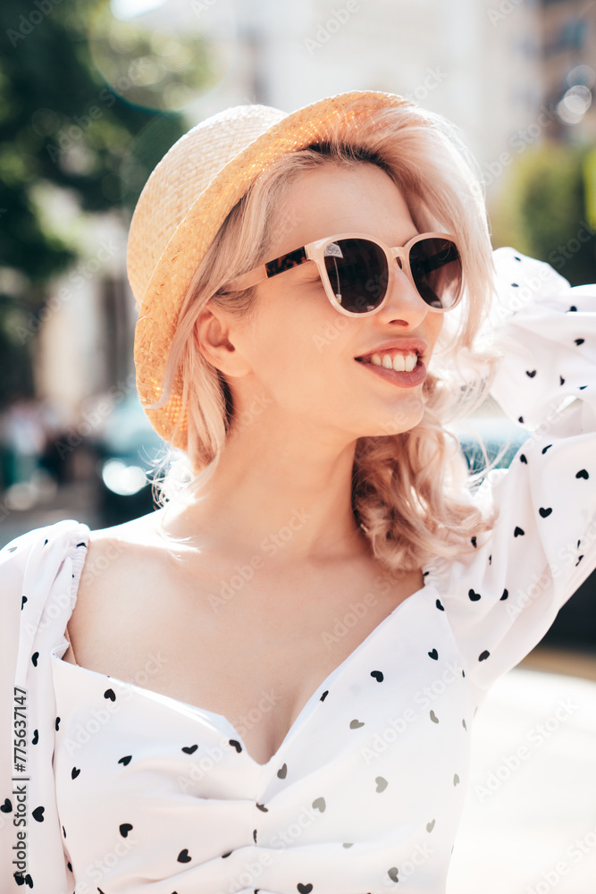 Young beautiful smiling blond woman in trendy summer yellow dress. Sexy carefree woman posing in street  at sunset. Positive model outdoors at sunny day. Cheerful and happy. In hat, sunglasses