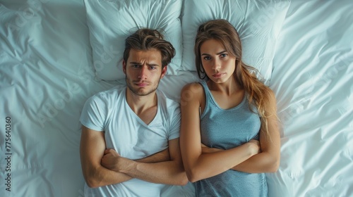 A young couple in bed, looking unhappy, with arms folded across their chests.