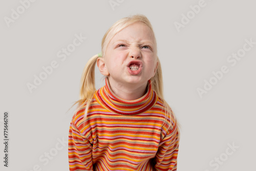 Cute little girl with blond hair in a striped t-shirt is yawning.