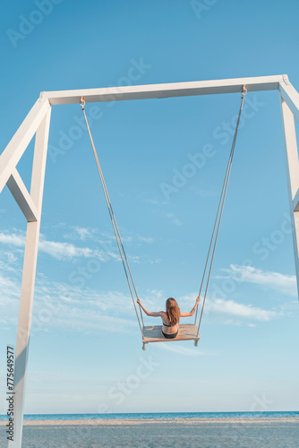 Girl with long hair on rope swing against on sea and blue sky background. Concept of freedom and child carelessness. Vertical frame.