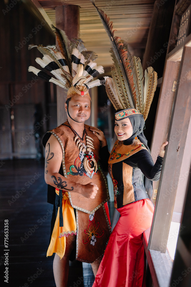Obraz premium Portrait of man and woman wearing traditional Kalimantan Dayak clothing with the background of a traditional Dayat house called