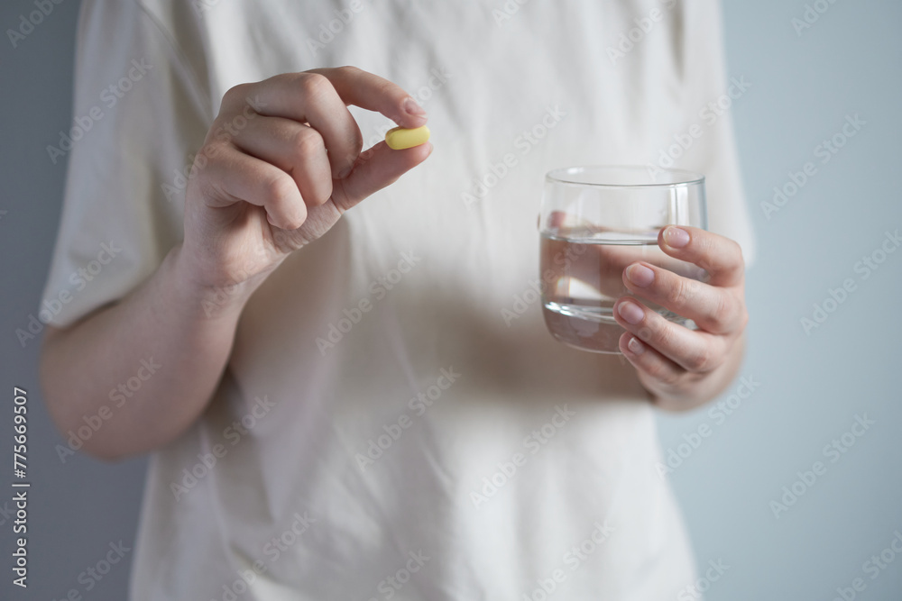 Woman holding a pill and a glass of water. Focus on pill