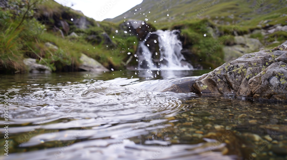 A tiny waterfall that cascades into a calm mountain stream and makes ripples in the crystal-clear water.