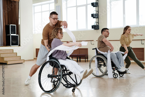 Group of four diverse men and women practicing dance with wheelchairs in studio, long shot