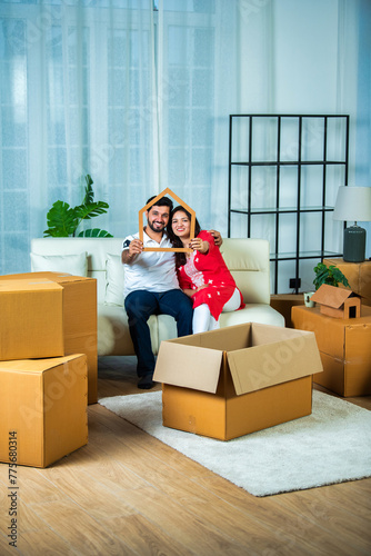 Indian couple holding piggy bank on home moving day  with cardboard boxes