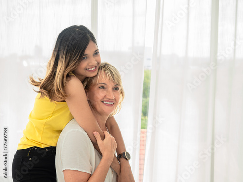 Portrait of Asian teen daughter is hugging her adopted caucasian mother looking at the camera and smile happily with each other. love and sharing time of stepmother, stepdaughter concept.