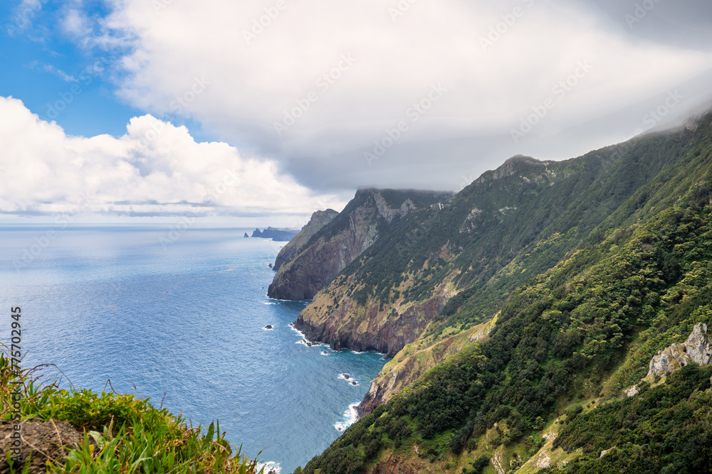Fototapeta premium A picturesque coastal landscape in Madeira. Visible are houses surrounded by greenery, mountains, and the azure sea. The harmony of nature and human habitation.