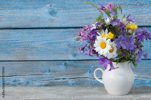 Bouquet of wildflowers in a white jug on a background of a blue wooden wall