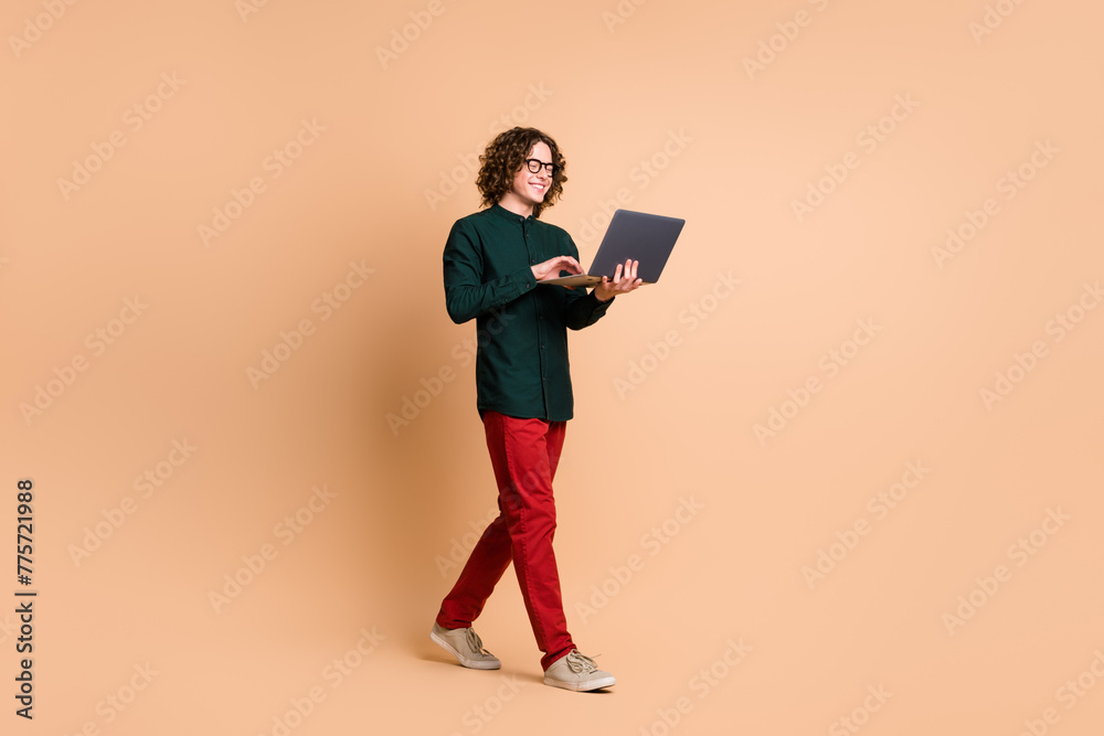 Photo portrait of handsome young guy eyewear hold netbook walk dressed stylish green garment isolated on beige color background Photo portrait of handsome young guy eyewear hold netbook walk dressed stylish green garment isolated on beige color background