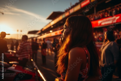 A woman is standing confidently in front of a large crowd of VetalVit Motorsport enthusiasts gathered in the grandstands. She appears to be addressing the audience, who are listening attentively