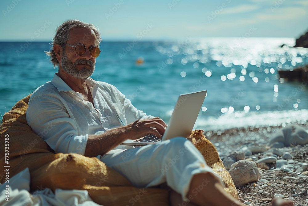 A mature man, enjoying the outdoors, works on his laptop at the beach, embracing modern technology