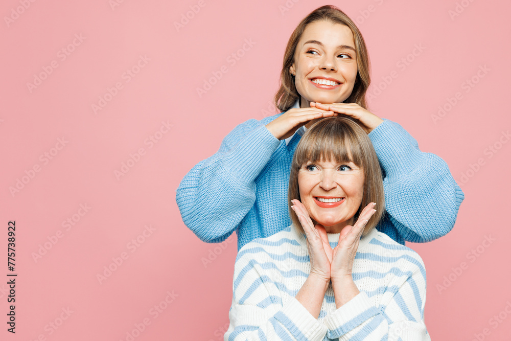 Elder parent mom 50s years old with young adult daughter two women together wear blue casual clothes stand behind mother hold hands on head isolated on plain light pink background. Family day concept. - obrazy, fototapety, plakaty 