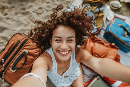 A portrait of a happy woman in the sand taking a selfie surrounded by luggage. Travel, vacation and free time concept. #775743138