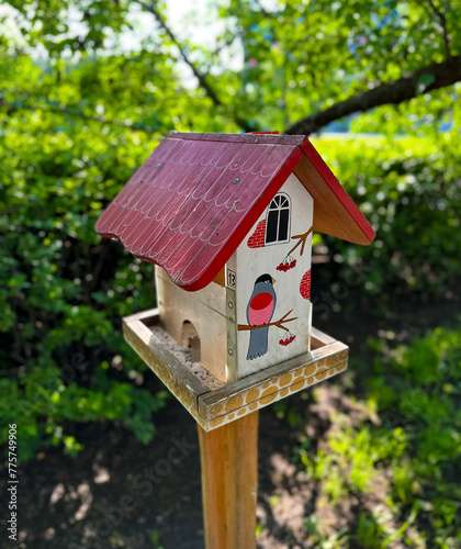 A hand-painted birdhouse with a vibrant red roof and illustrations of birds, perched outdoors with a lush green background © DmitriiArtamonov