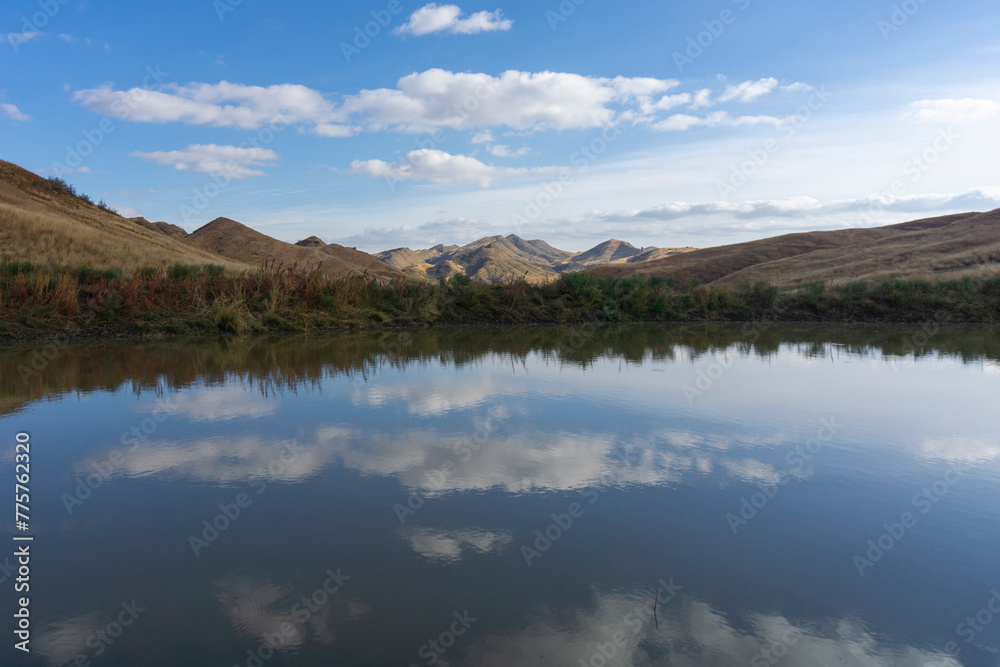 Beautiful view of the lake and mountains. Bright blue sky. Clouds are reflected in the water. Orange dry grass. Desert region of Georgia.