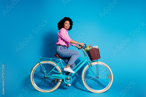 Full size side profile photo of cute woman wear pink shirt jeans pants driving bicycle to empty space isolated on blue color background © deagreez