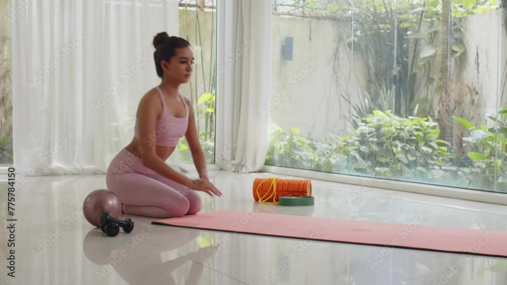 Wide shot of young Asian gen Z sportswoman rolling out yoga mat while working out indoorsWide shot of young Asian gen Z sportswoman rolling out yoga mat while working out indoors