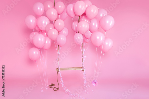 Romantic swing decorated with bunch of pink balloons on a pink background in the studio. Birthday and wedding celebration concept. Decor for holidays and events.