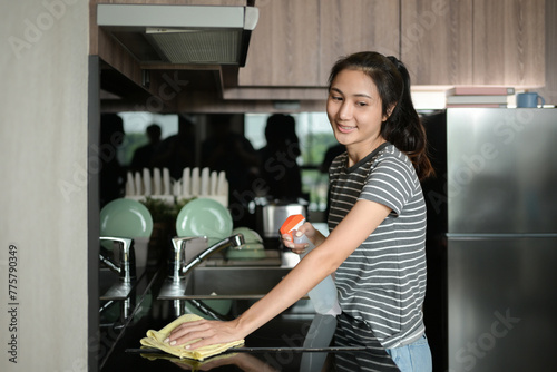 Young housewife wearing rubber gloves cleaning electric stove with spray bottle and microfiber cloth