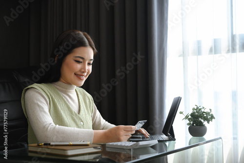Attractive young woman holding credit card and calculating monthly expenses at home