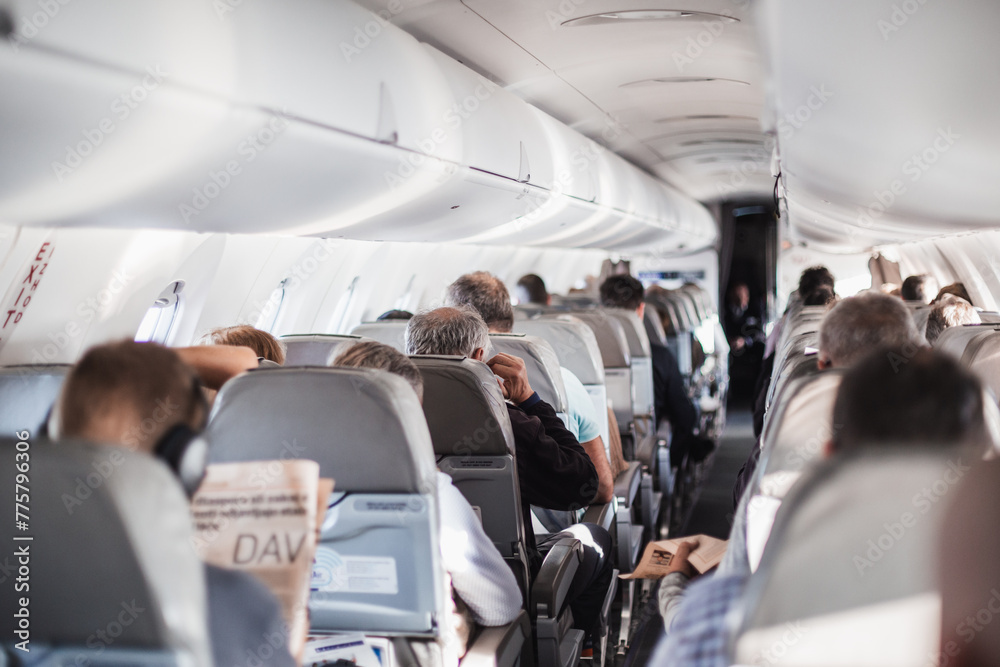 Interior of airplane with passengers on seats and stewardess in uniform walking the aisle, serving people. Commercial economy flight service concept