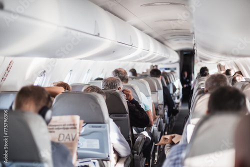 Interior of airplane with passengers on seats and stewardess in uniform walking the aisle, serving people. Commercial economy flight service concept