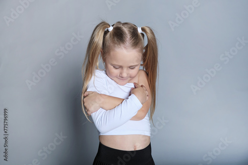 Young girl hugs herself, a shy smile on her face. Evokes self-love and the comfort found in one's own embrace.
