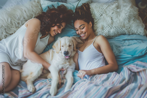 A lesbian couple wrapped up peacefully in their bed, enjoying a morning of games and fun with their friendly dog. Concept of life as a couple, pets, home.