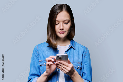 Young serious woman using smartphone in gray studio background