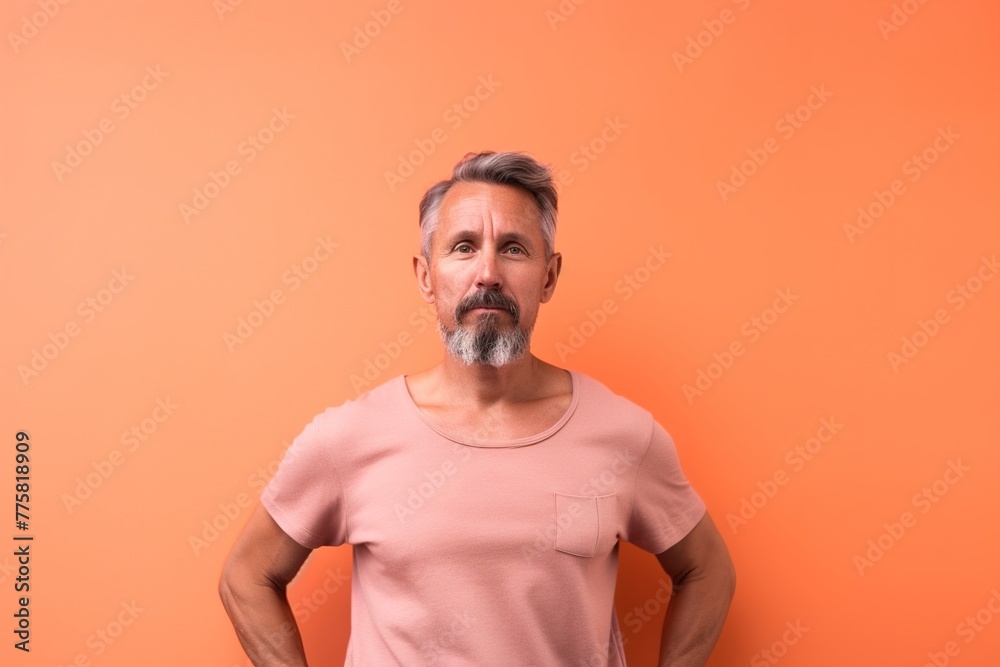 A man with a beard and gray hair is standing in front of a bright orange wall