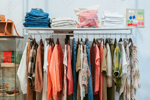 A colorful assortment of clothing items, including denim and patterned apparel, displayed on a metal rack with neatly folded piles on top photo
